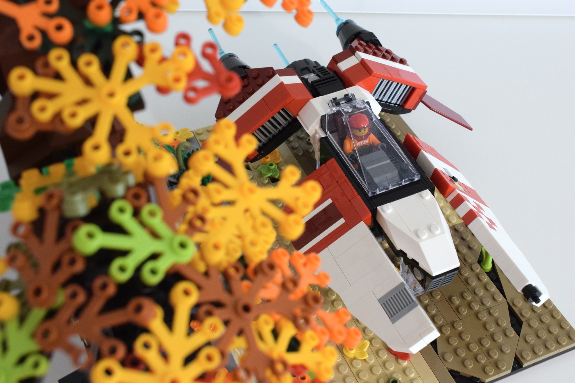 The racing vehicle is partially obscured by the yellow leaves of the tree in the diorama. The vehicle is a narrow central hull with mirrored narrow wings up front and two large engine intakes mounted behind the cockpit.