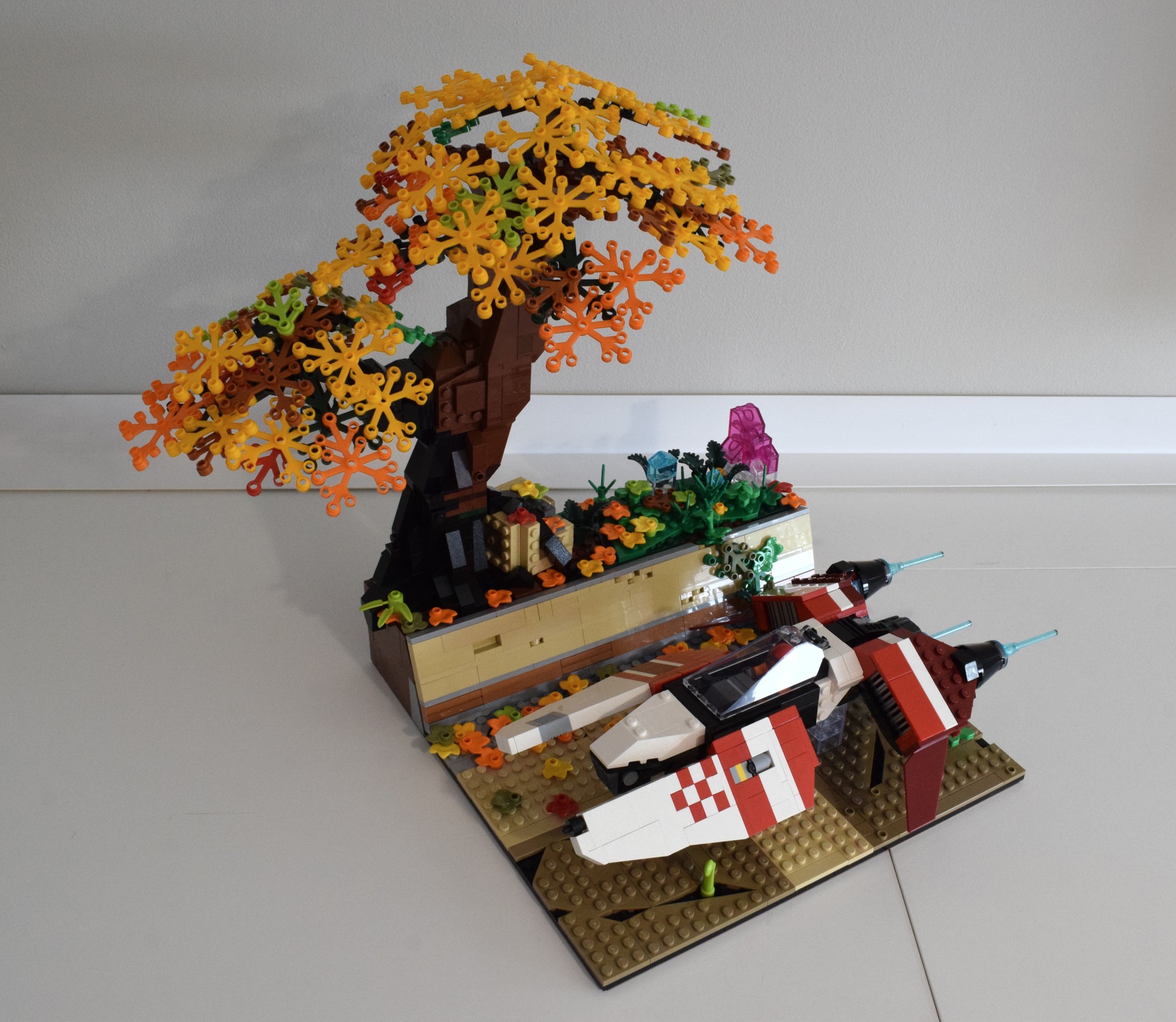Lego diorama depicting a futuristic hover racing vehicle racing through a cracked stone-brick valley. A great tree clad in autumnal leaves is snaking its roots down the side of the ancient masonry.